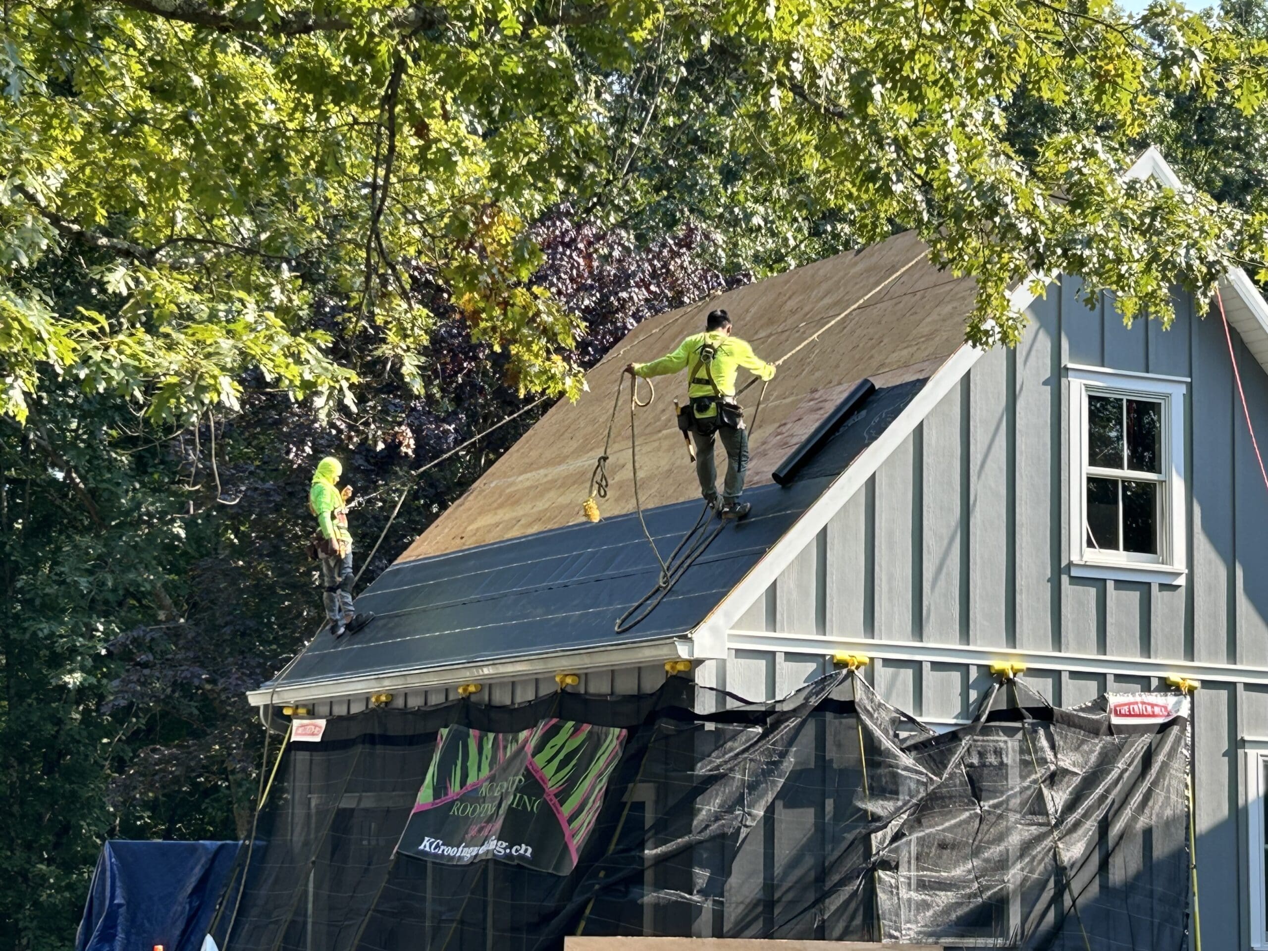Roofing contractors on a residential roof using best practices for safety by being attached to harnesses