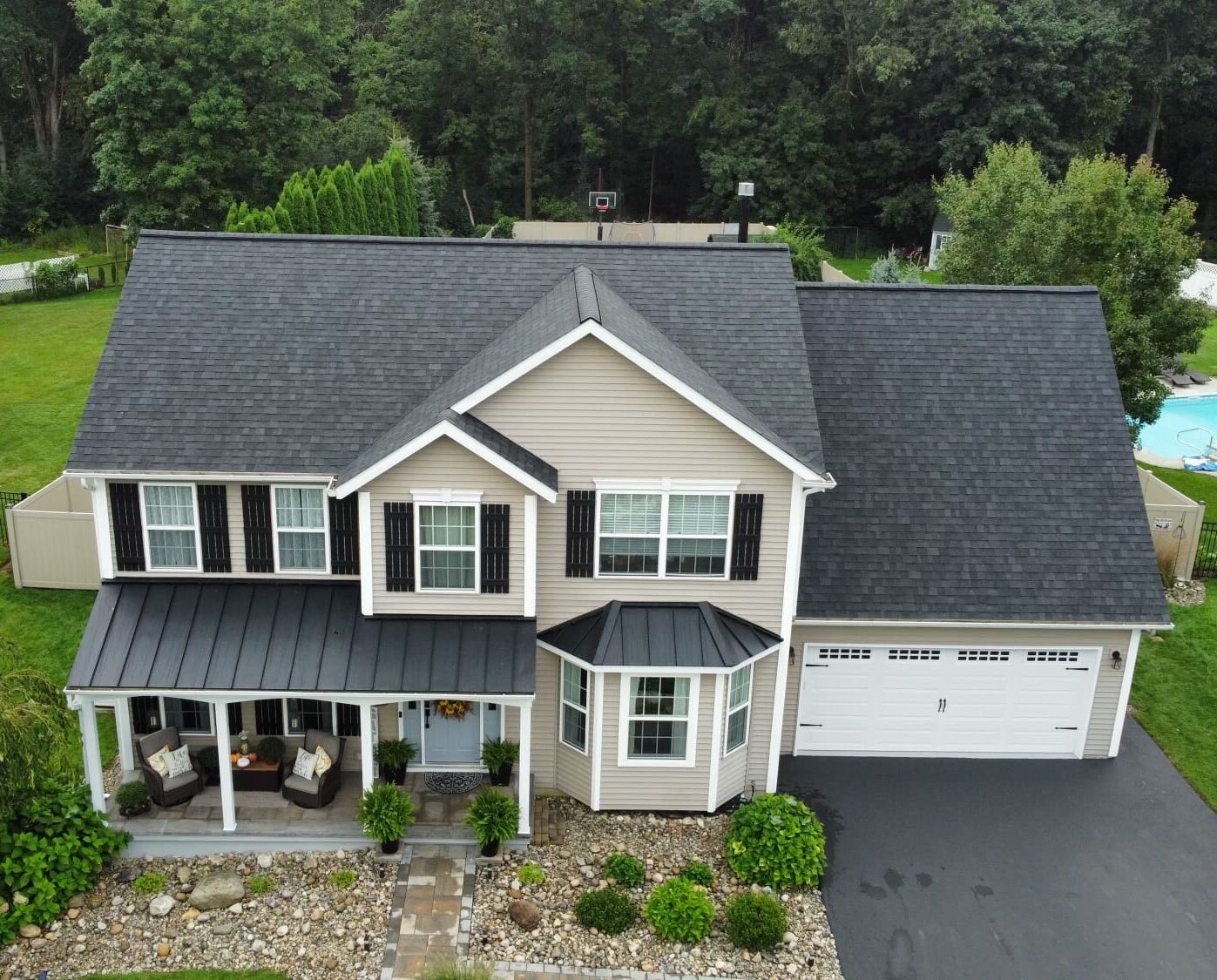 View of a residential house with newly replaced roof with Owens Corning Onyx Black asphalt shingles and black metal roofing on the awnings over the porch and bay window