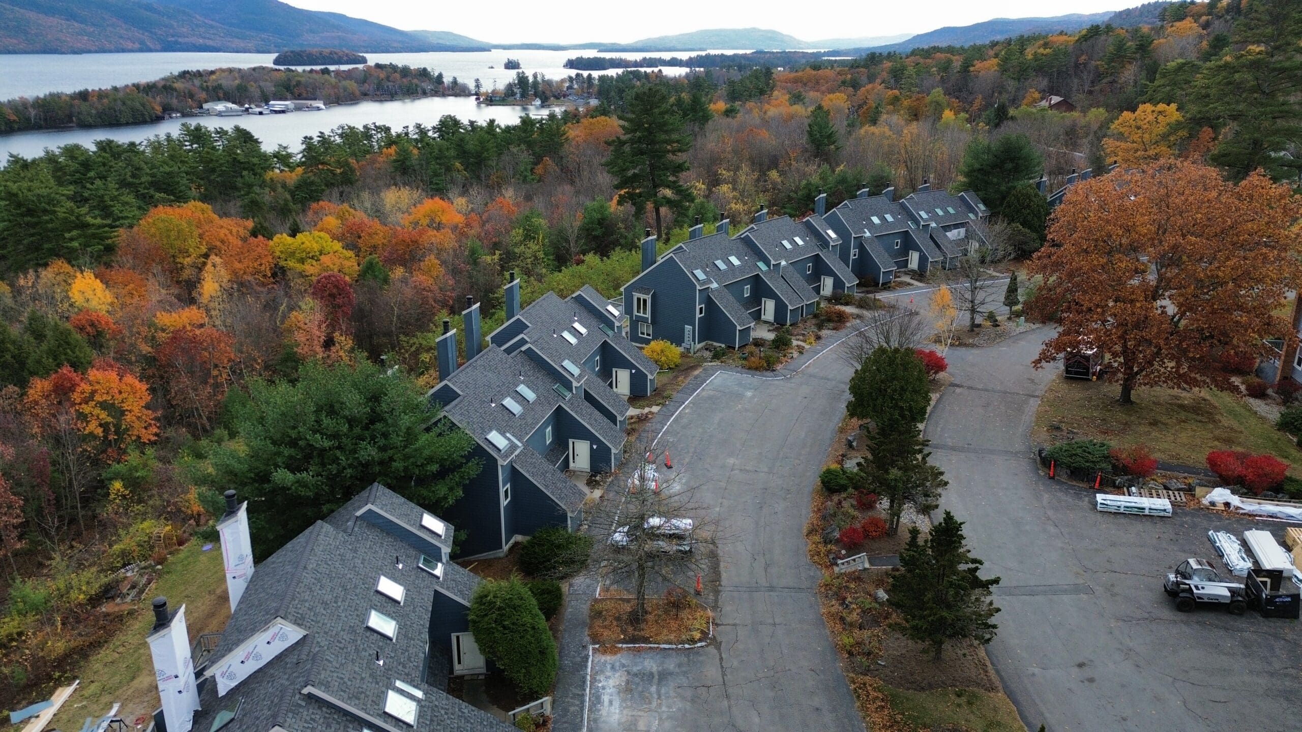 Aerial image of condos with roof replacements done by KC Entities Roofing and Siding, with trees with red and orange leaves and a view of Lake George